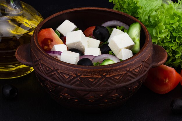 Ensalada griega con verduras frescas, queso feta y aceitunas negras sobre un fondo oscuro.