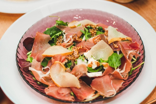 Ensalada con hierbas, rúcula, prosciutto, queso, aceitunas verdes y nueces.