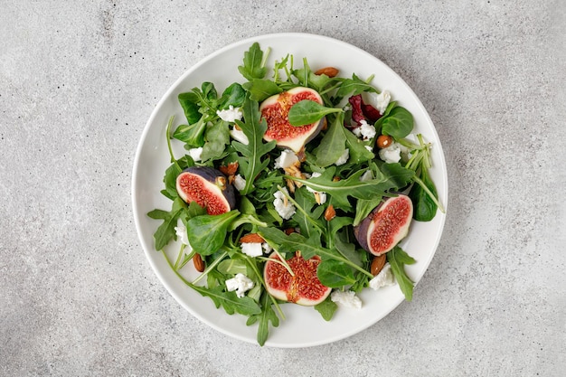 Ensalada con higos, rúcula, queso feta en un plato blanco sobre fondo gris Ensalada de higos de otoño Vista superior