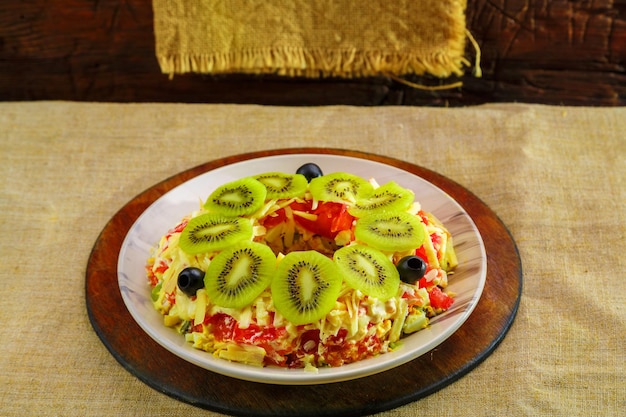 Ensalada de hojaldre con pechuga de pollo, adornada con kiwi y aceitunas en una ensaladera sobre un mantel. foto horizontal