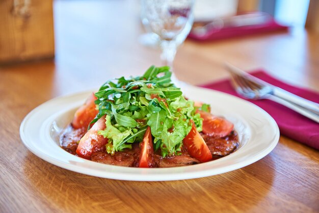 Ensalada con hojas de rúcula, carne frita y tomate en la mesa