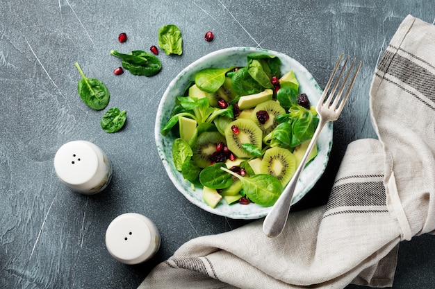 Ensalada de hojas tiernas de espinacas, berros, kiwi, aguacate y granada en un plato de cerámica antigua sobre un fondo de hormigón gris