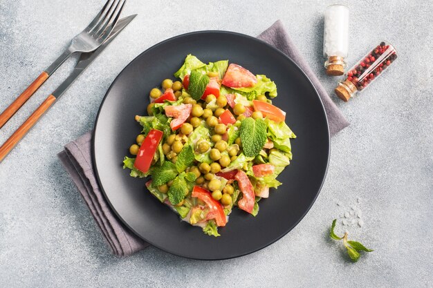 Ensalada de hojas de tomate verde y guisantes enlatados condimentados con salsa sobre un plato negro. Ensalada de dieta fresca de primavera. vista superior