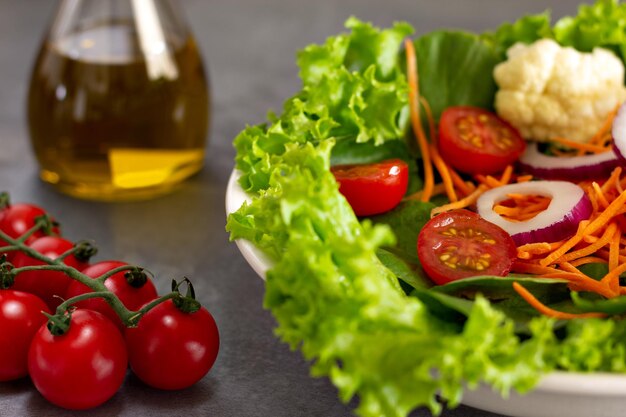 Ensalada de hojas verdes con coliflor de cebolla tomate zanahoria con vaso de aceite de oliva en el fondo