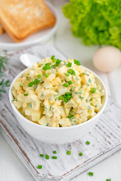 Ensalada de huevo con cebollas verdes picadas encima en un tazón blanco para cocinar un sándwich Enfoque selectivo