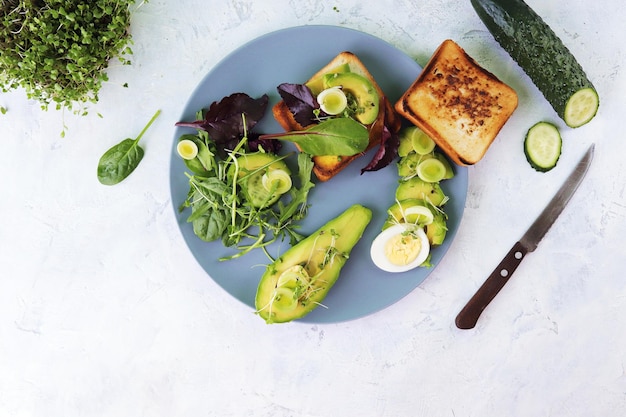 Ensalada de huevos cocidos con aguacate puerro micro brotes verdes y rúcula en un plato sobre una mesa de luz