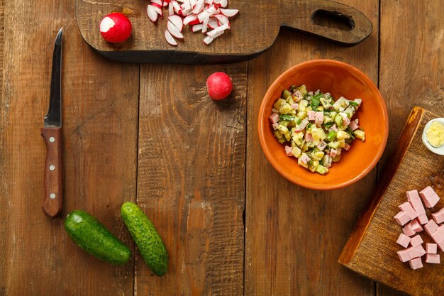 Ensalada de ingredientes en un recipiente y sobre tablas de cortar sobre fondo de madera, vista superior