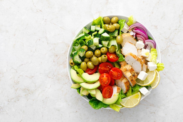 Ensalada de inspiración griega con verduras de carne de pollo a la parrilla y queso feta en un bol sobre una mesa con vista superior de aderezo de aceite de oliva