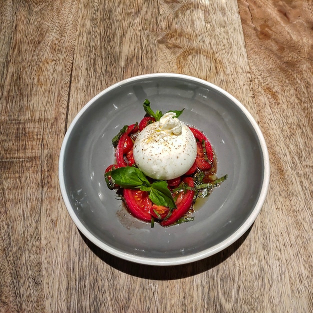 Foto ensalada italiana tradicional con queso burrata, tomates y albahaca fresca se encuentra en una placa gris.