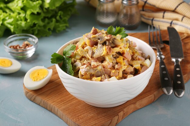 Ensalada de jamón, huevos, cebolla y champiñones en un recipiente blanco sobre tabla de madera