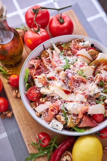 Ensalada con jamón o prosciutto peras tomates y rúcula sobre tabla de madera