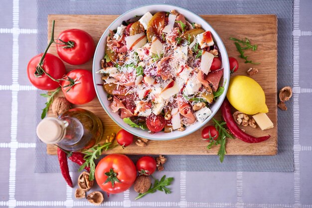 Ensalada con jamón o prosciutto peras tomates y rúcula sobre tabla de madera