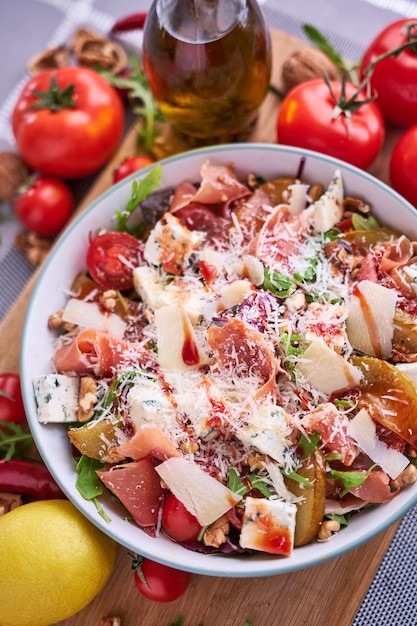 Ensalada con jamón o prosciutto peras tomates y rúcula sobre tabla de madera