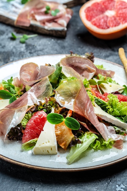 Ensalada de jamón prosciutto crudo con queso brie camembert y pomelo, mezcla de ensalada. Menú de restaurante, dieta, receta de libro de cocina.