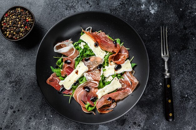 Ensalada de jamón prosciutto crudo con queso brie camembert y rúcula en un plato.