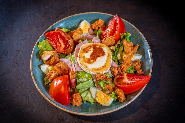 Ensalada de jamón, queso y pollo sobre un fondo negro, sobre una placa verde