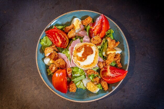 Ensalada de jamón, queso y pollo sobre un fondo negro, sobre una placa verde