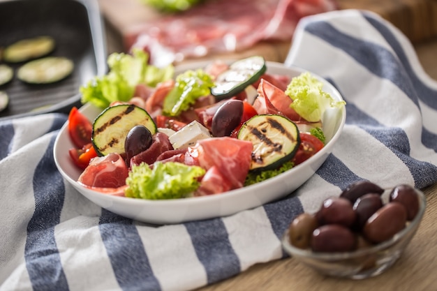 Ensalada de lechuga fresca con calabacín a la plancha, coppa di parma, jamón, queso feta, aceitunas, tomates y aceite de oliva.