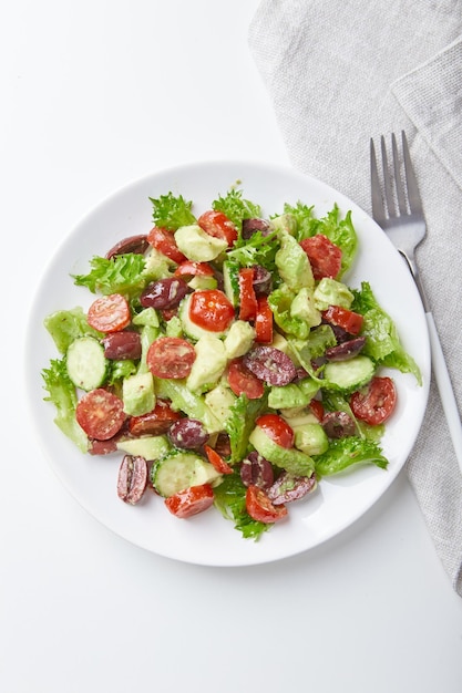 Ensalada con lechuga pepinos tomates aceitunas y aguacates en plato blanco sobre la mesa