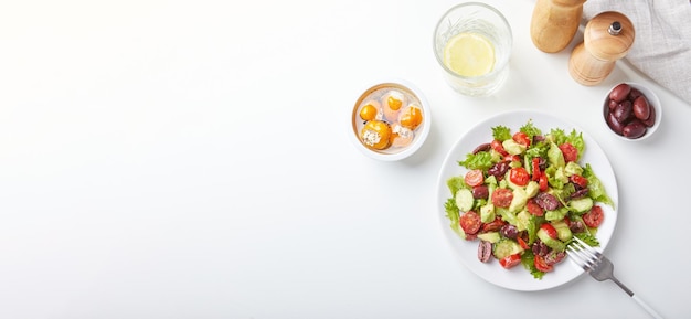 Ensalada con lechuga pepinos tomates aceitunas y aguacates en plato blanco sobre la mesa