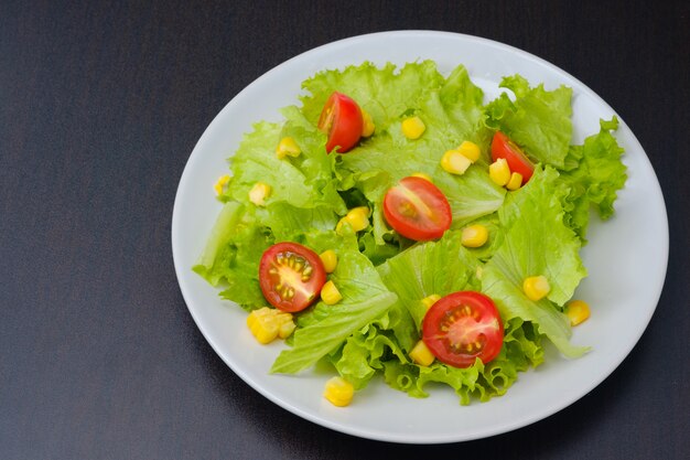 Ensalada de lechuga y tomate cherry, naranja, maíz en un plato blanco. Concepto para una comida sabrosa y saludable. Concepto de comida vegetariana