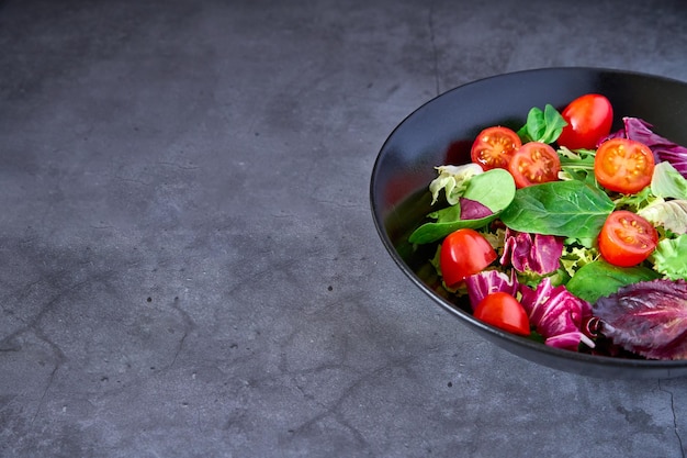 Una ensalada de lechuga, tomate, cordero, lechuga y escarola en un plato negro sobre un fondo de pizarra