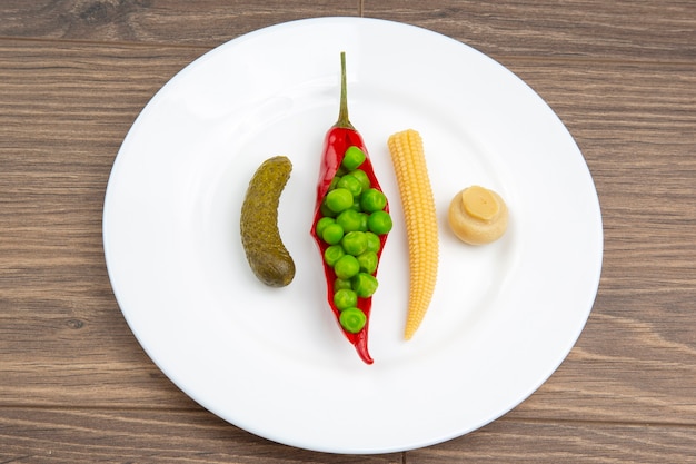 Ensalada de maíz en escabeche y encurtidos, guisantes, pepino y pimiento rojo en un plato blanco.