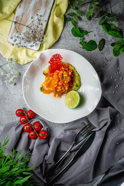 Ensalada de mango y salmón con salsa y puré de aguacate y lima en un plato sobre una mesa de piedra gris. Menú del restaurante