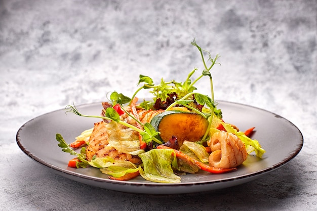 Ensalada de mariscos con calamares a la plancha, maíz, zanahorias, tomates y lechuga, sobre una placa gris