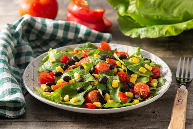 Ensalada mexicana con frijoles negros, maíz, tomate, lechuga y pimiento en mesa de madera