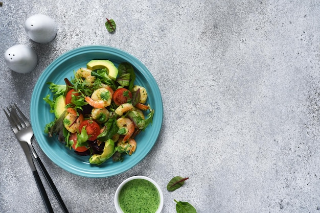 Ensalada de mezcla verde con tomates y camarones y salsa sobre un fondo de hormigón Vista desde arriba