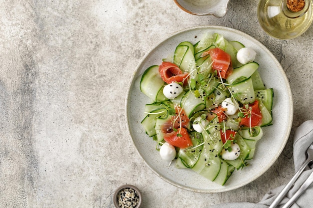 Ensalada con microgreens de queso mozzarella de pepinos en rodajas de salmón en placa de cerámica gris