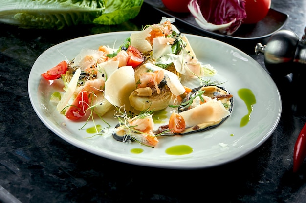 Ensalada mixta con camarones a la plancha, parmesano y alcachofa servida en un plato blanco sobre una mesa de mármol oscuro. Comida de restaurante.