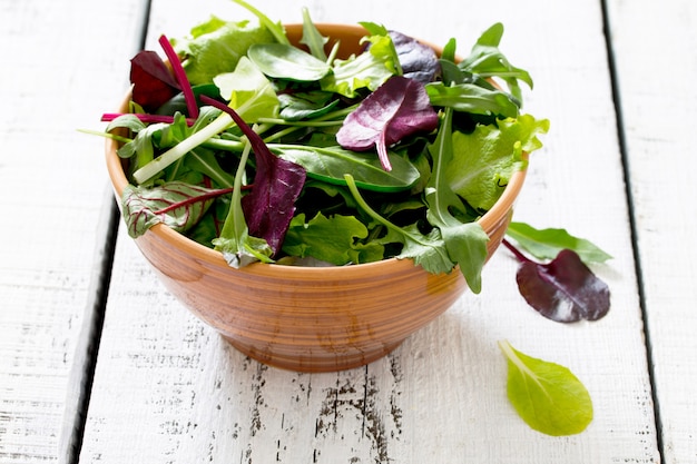 Ensalada mixta verde fresca en un recipiente sobre una mesa de madera