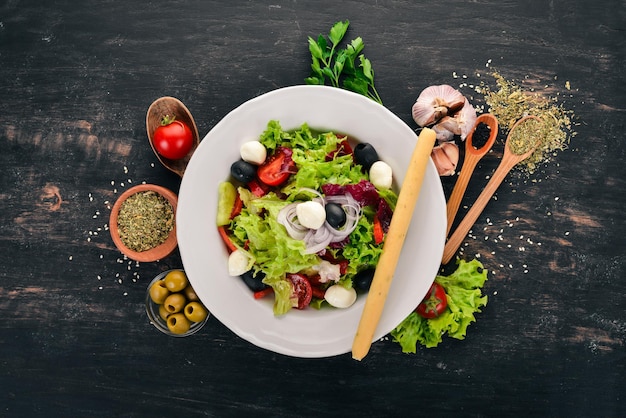 Ensalada con mozzarella y verduras frescas. Sobre un fondo de madera negra. Vista superior. Copie el espacio para su texto.