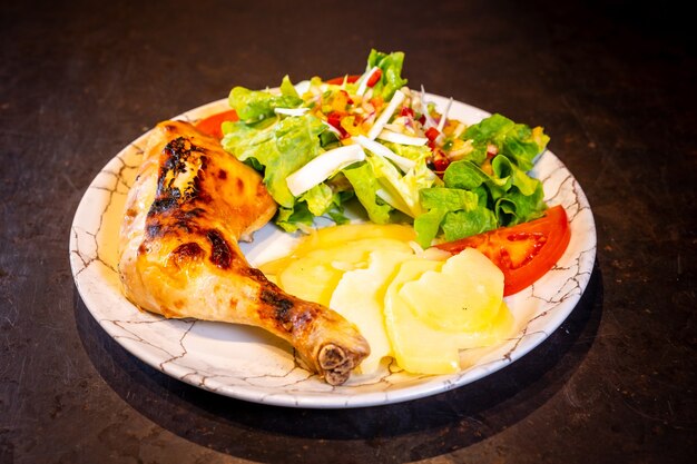 Ensalada de muslo de pollo y ensalada sobre un fondo negro, sobre una placa blanca.