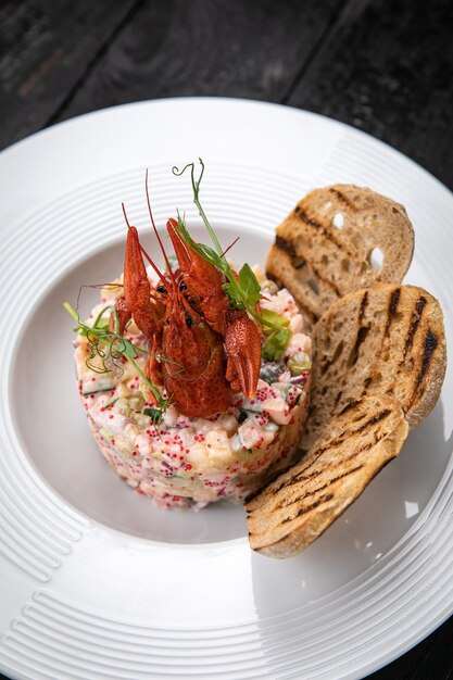 Ensalada Olivier con mariscos y caviar sobre una mesa oscura