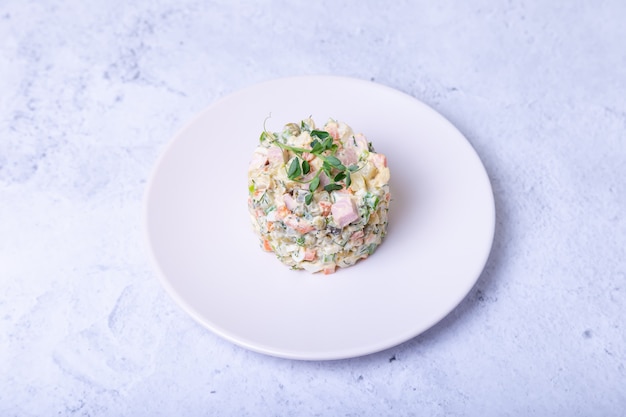 Ensalada Olivier en un plato blanco, decorada con brotes de guisantes.