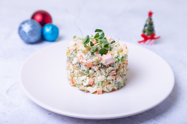 Ensalada Olivier en un plato blanco, decorado con brotes de guisantes. Ensalada rusa tradicional de Año Nuevo y Navidad. Primer plano, enfoque selectivo, fondo blanco.