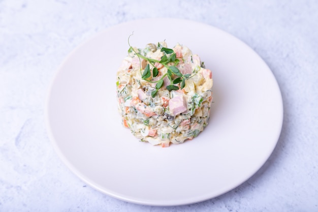 Ensalada Olivier en un plato blanco, decorado con brotes de guisantes. Ensalada rusa tradicional de Año Nuevo y Navidad. Primer plano, enfoque selectivo.