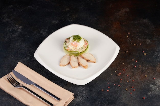 Ensalada Olivier servida sobre hojas de espinaca en un plato cuadrado blanco