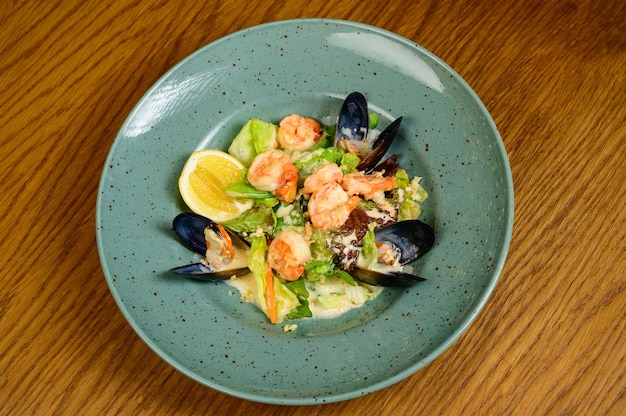 Foto ensalada de ostras, camarones y verduras en placa azul sobre fondo de madera, vista superior