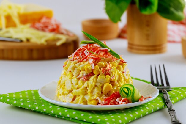 Ensalada con palitos de cangrejo, huevos de pepino y chips de maíz en placa verde con tenedor