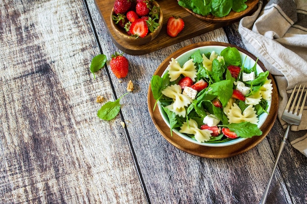 Ensalada de pasta italiana con fresas, rúcula, nueces, queso suave vestido con espacio de copia