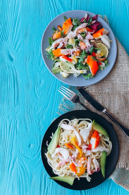 ensalada y pasta con mariscos sobre un fondo azul