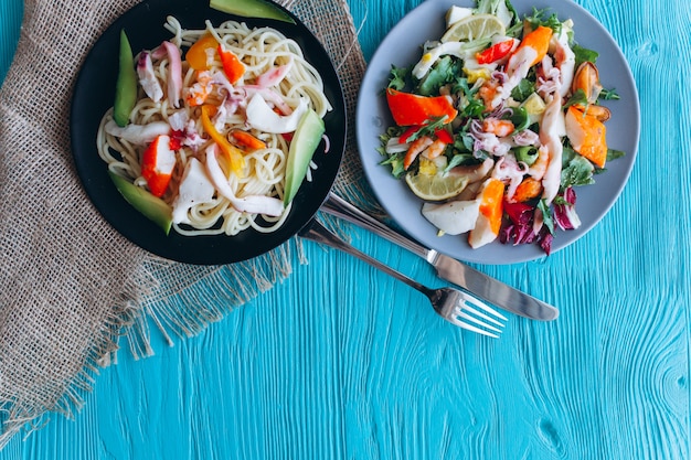 ensalada y pasta con mariscos sobre un fondo azul