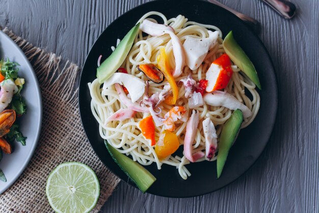 ensalada y pasta con mariscos sobre fondo de madera