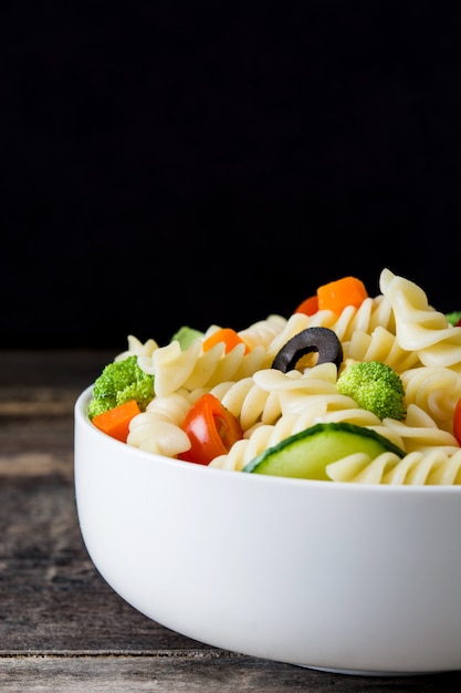 Ensalada de pasta en un recipiente en la mesa de madera