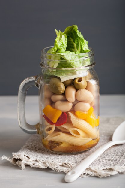 Ensalada de pasta vegana en tarros de albañil con verduras, frijoles, aceitunas