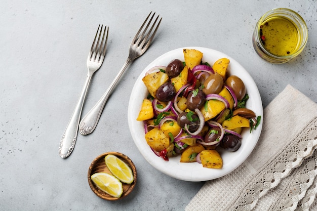 Ensalada de patata caliente con aceitunas, pimiento, perejil y cebolla roja sobre placa de cerámica blanca antigua